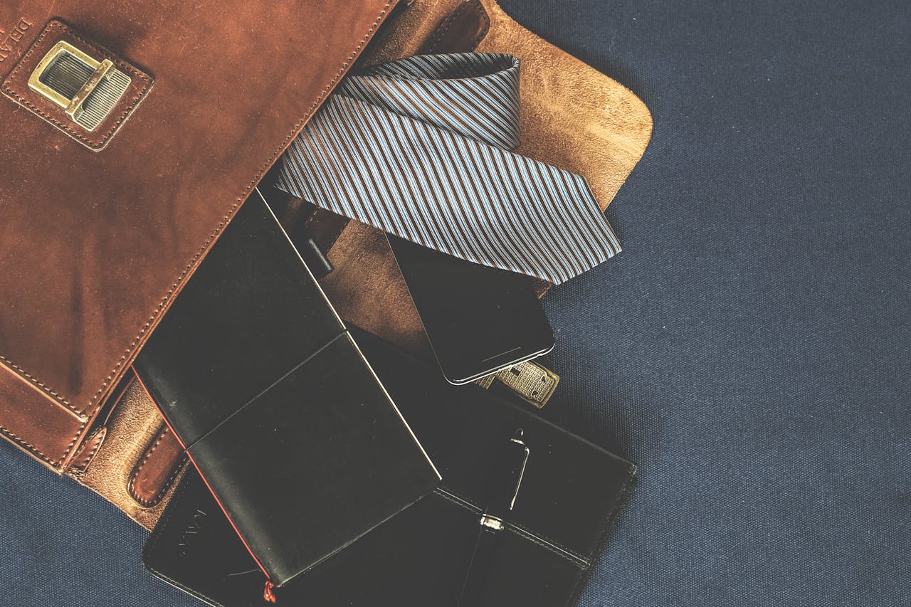 Flat lay of mens leather bag with accessories like a tie, notebook, and phone. Ideal for business themes.
